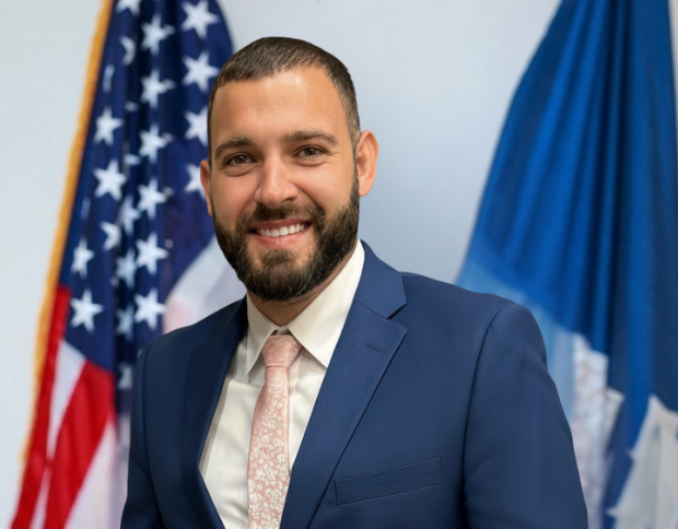 Portrait of Blake Pohlmann Buras, Director of Security and Vessels, smiling in a navy suit and light pink tie.