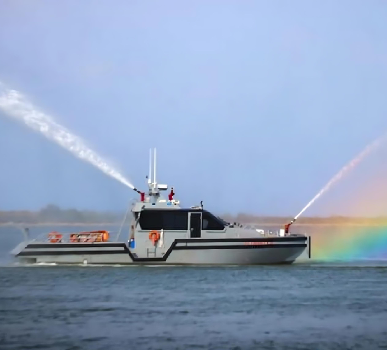 Fireboat sprays high arcs of water from its cannons, creating a small rainbow over the water.