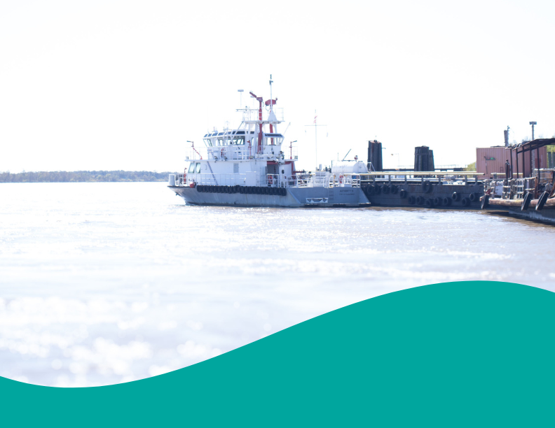 White and gray ferry or work vessel docked on a bright, sunny day with sparkling water.