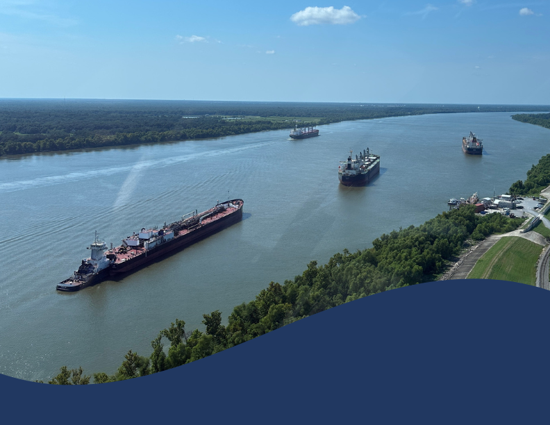 Aerial view of large commercial vessels navigating the Mississippi River, surrounded by green trees.