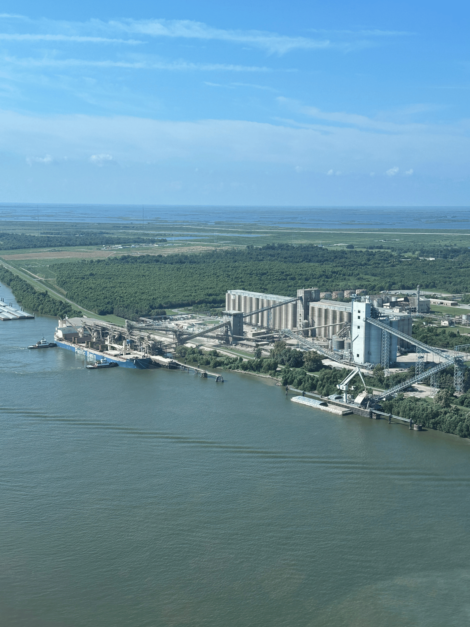 Aerial view of a massive grain elevator and terminal facility on the river, with a ship docked for loading.