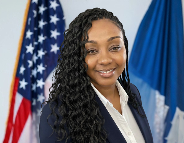 Portrait of Trenise Jones, smiling in a navy blazer with the American flag visible in the background.